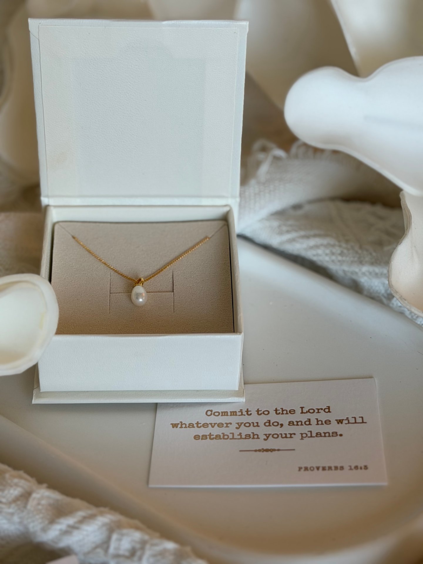 A pearl necklace in an open gift box beside a Proverbs 16:3 card
